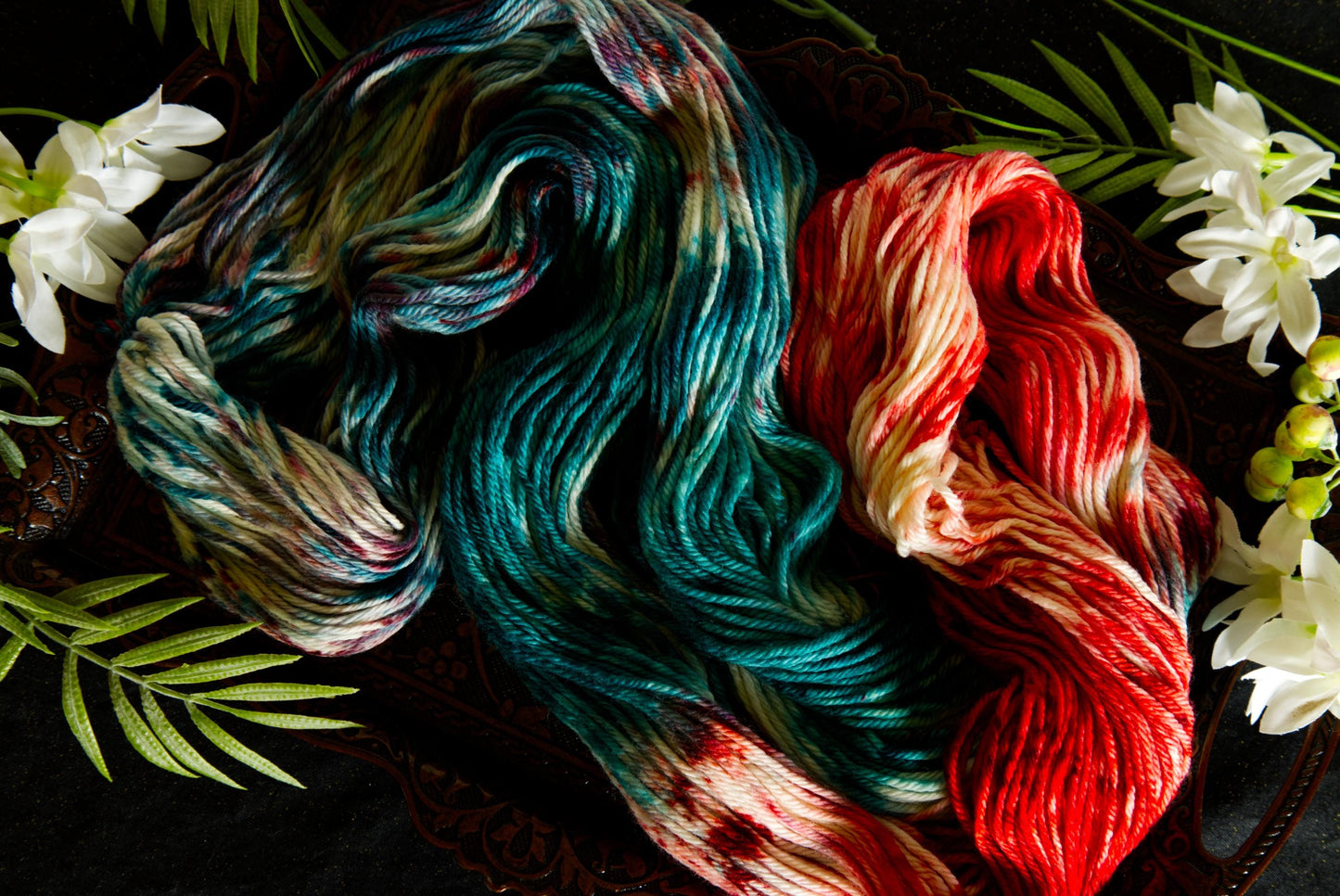 A hank of hand dyed yarn lays spread out on a table, surrounded by flowers. It is red, green, and white.