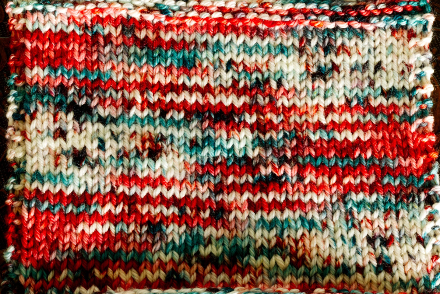 A close up of a knit swatch, showing off the color detail of hand dyed yarn. It is red, white, and green striped.