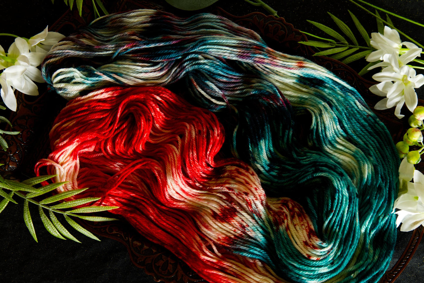 A hank of hand dyed yarn lays spread out on a table, surrounded by flowers. It is red, green, and white.