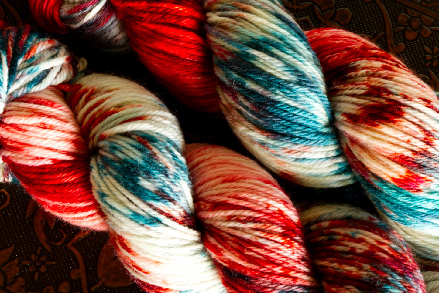 A close up of two skeins of yarn that are hand dyed green, red, and white. The close up shows off the beautiful color pooling and texture of the yarn.